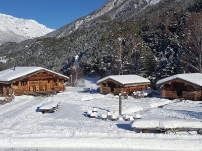 Chalets en bois dans un paysage enneigé, entourés de montagnes majestueuses.