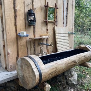 Cabane en bois avec un lavabo en rondins et une lampe à huile, au cœur de la nature.