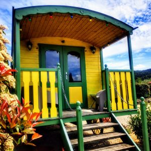 Roulotte colorée avec balustrade jaune, entourée de verdure en Auvergne-Rhône-Alpes.