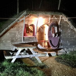 Hébergement insolite : une cabane en bois avec une porte ronde et un éclairage chaleureux.