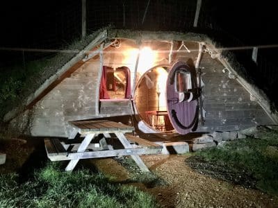 Hébergement insolite : une cabane en bois avec une porte ronde et un éclairage chaleureux.