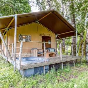 Tente safari spacieuse avec terrasse en bois et jacuzzi, entourée de verdure.