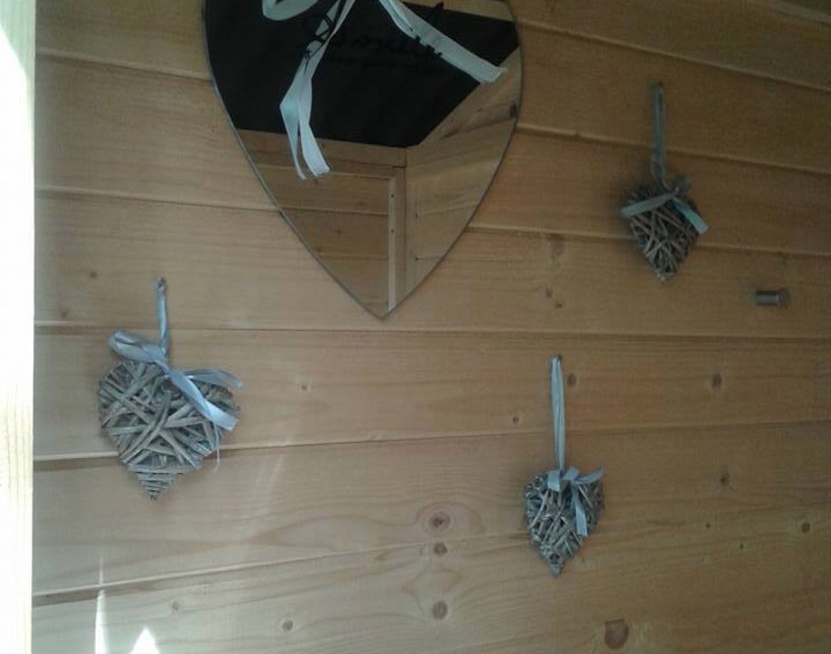 Cabane en bois avec miroir en cœur et décorations en osier, ambiance chaleureuse.