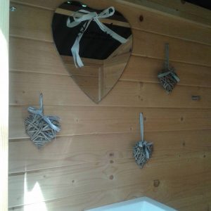 Cabane en bois avec miroir en cœur et décorations en osier, ambiance chaleureuse.