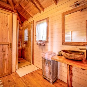 Salle de bain dun hébergement insolite en bois, avec un lavabo en pierre et une douche.