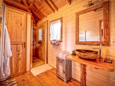 Salle de bain dun hébergement insolite en bois, avec un lavabo en pierre et une douche.