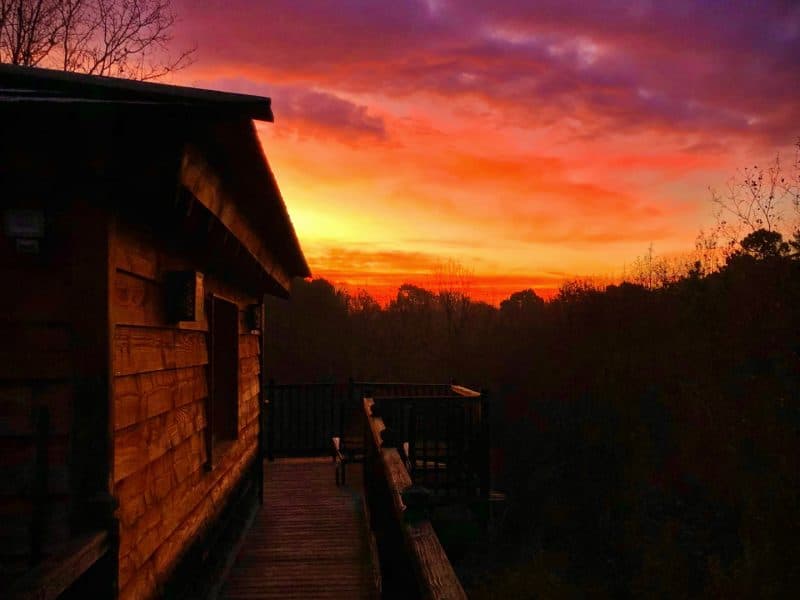 Cabane en bois avec un balcon, face à un magnifique coucher de soleil coloré.
