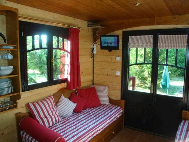 Chalet en bois cosy avec canapés rayés et vue sur la verdure extérieure.
