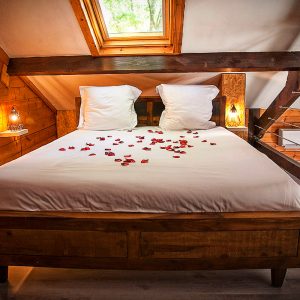 Chalet en bois avec lit décoré de pétales de roses, ambiance romantique et chaleureuse.