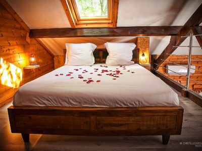 Chalet en bois avec lit décoré de pétales de roses, ambiance romantique et chaleureuse.