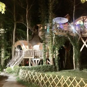 Cabane perchée illuminée, entourée darbres, offrant une expérience unique en Île-de-France.