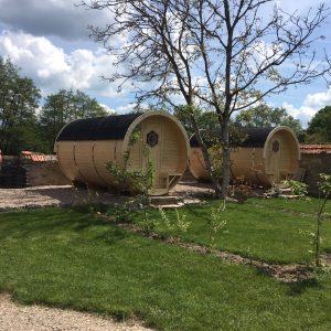 Hébergement insolite en tonneaux en bois, entouré de verdure et darbres.
