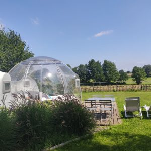 Hébergement insolite en bulle transparente, avec vue sur la verdure et chaises longues.