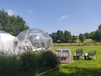 Hébergement insolite en bulle transparente, avec vue sur la verdure et chaises longues.