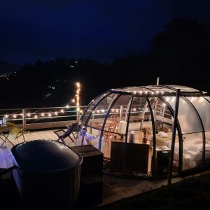 Hébergement insolite en bulle transparente, illuminée, avec vue nocturne sur la vallée.