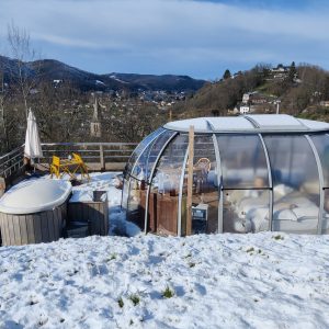 Hébergement insolite en bulle transparente avec jacuzzi, entouré de neige et montagnes.