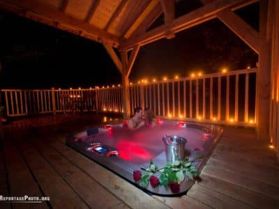Cabane en bois avec jacuzzi romantique, éclairage doux et roses sur la terrasse.