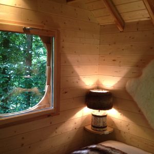 Cabane perchée en bois avec vue sur la forêt et lumière douce.