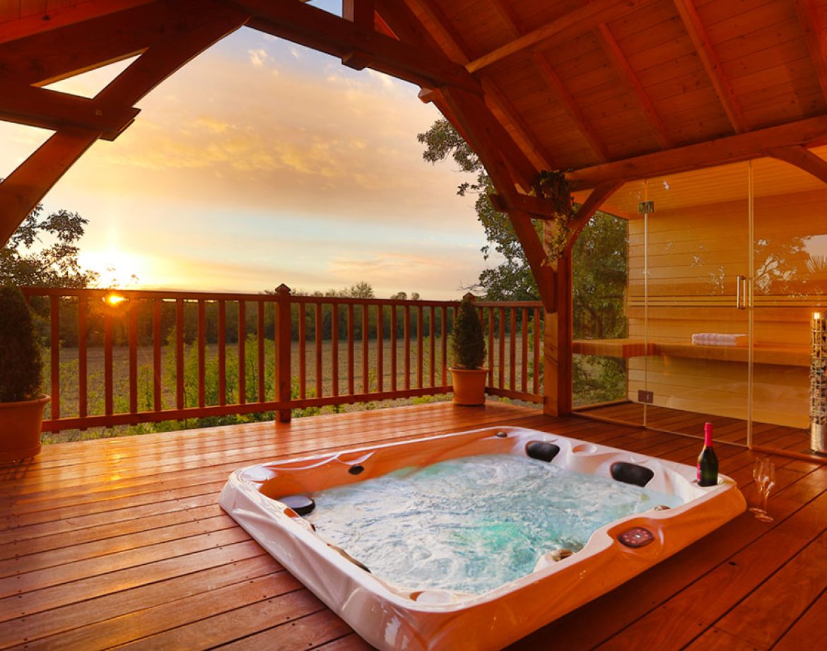 Cabane en bois avec jacuzzi extérieur, vue sur le coucher de soleil.