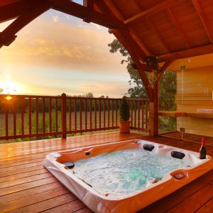 Cabane en bois avec jacuzzi extérieur, vue sur le coucher de soleil.