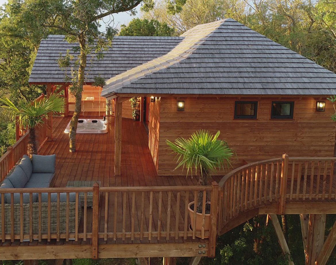 Cabane perchée en bois dans les arbres, avec terrasse et jacuzzi.