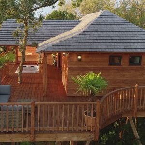 Cabane perchée en bois dans les arbres, avec terrasse et jacuzzi.