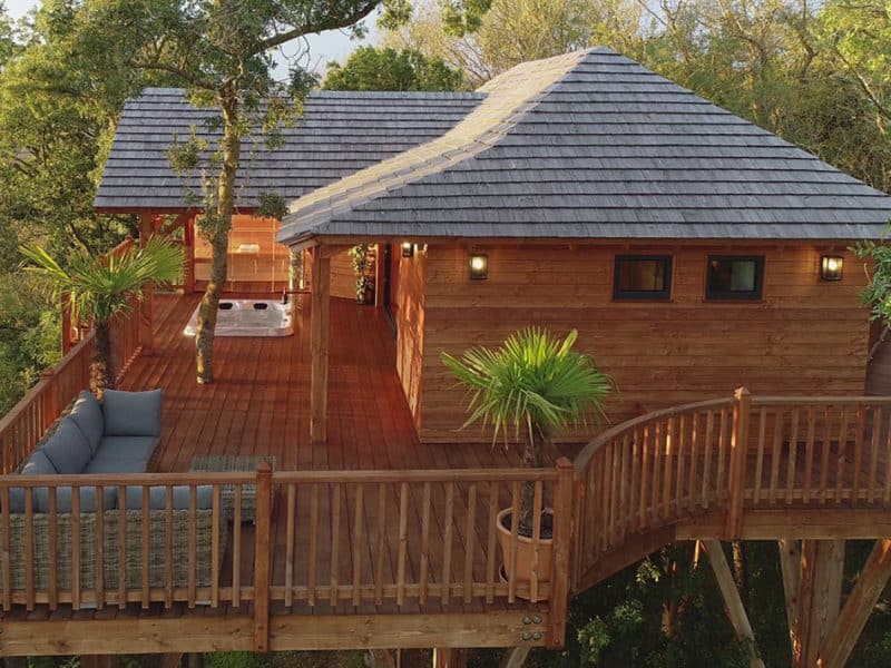 Cabane perchée en bois dans les arbres, avec terrasse et jacuzzi.