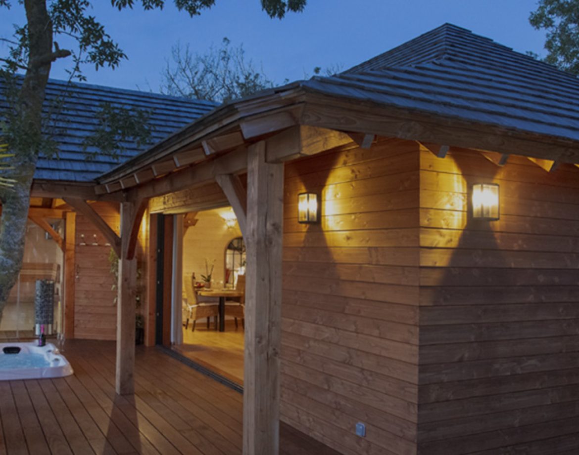 Cabane en bois avec jacuzzi, entourée de verdure au crépuscule.