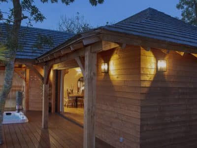 Cabane en bois avec jacuzzi, entourée de verdure au crépuscule.