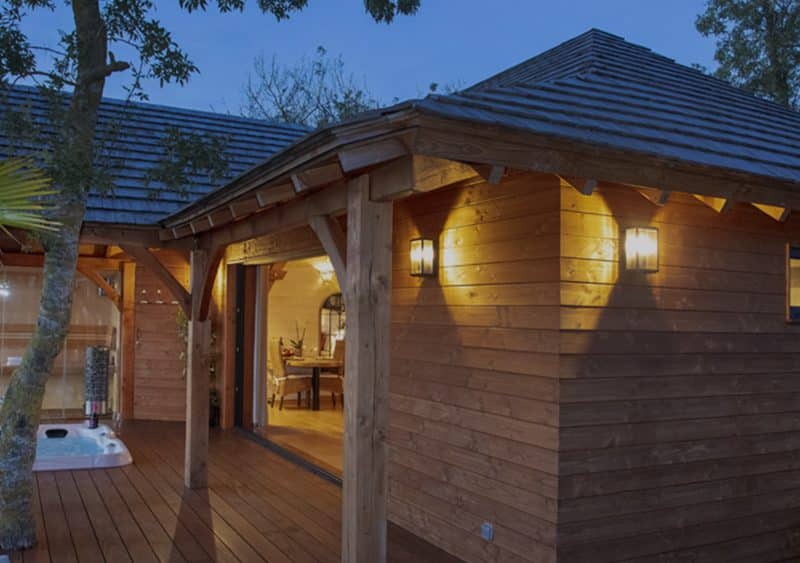 Cabane en bois avec jacuzzi, entourée de verdure au crépuscule.