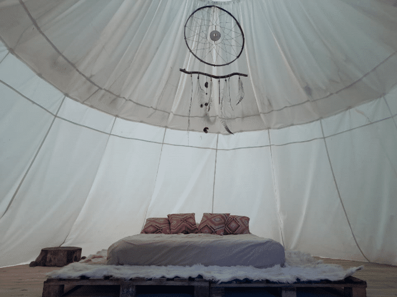 Tente de glamping avec un lit douillet et des coussins colorés, ambiance cosy.