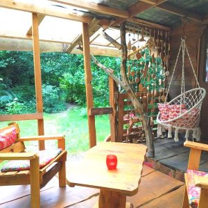Cabane en bois à Basse-Normandie, avec fauteuils colorés et hamac suspendu.