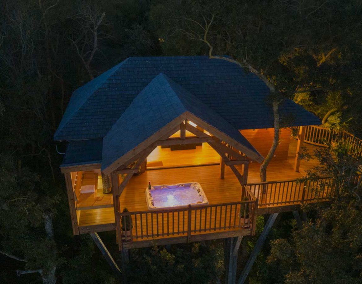 Cabane perchée dans les arbres avec jacuzzi, illuminée au crépuscule.