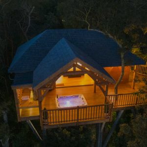 Cabane perchée dans les arbres avec jacuzzi, illuminée au crépuscule.