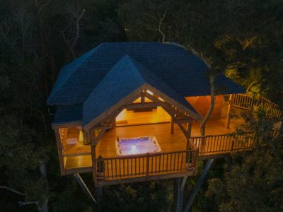 Cabane perchée dans les arbres avec jacuzzi, illuminée au crépuscule.