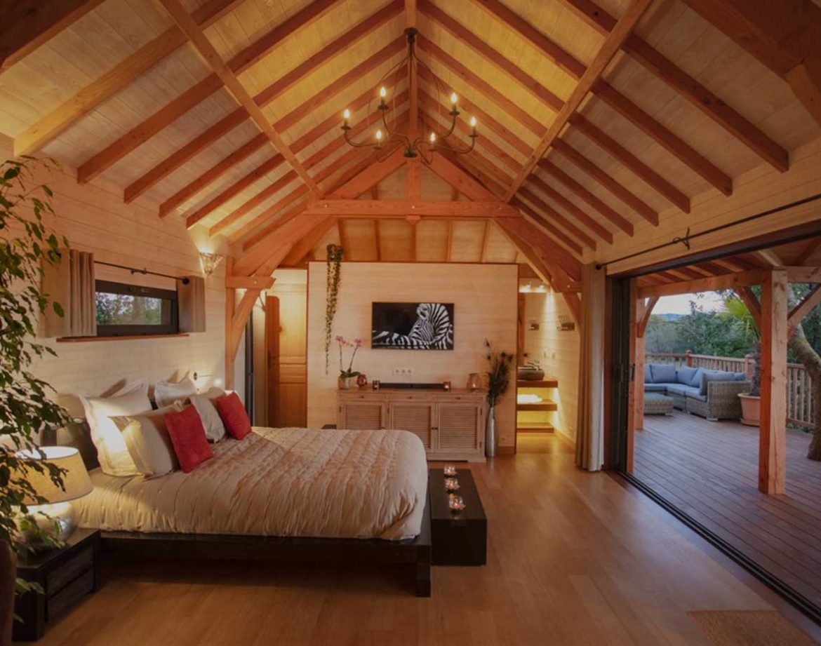 Chalet en bois avec lit douillet et grandes baies vitrées sur la terrasse.