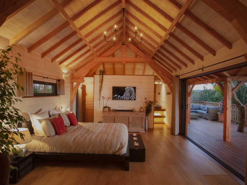 Chalet en bois avec lit douillet et grandes baies vitrées sur la terrasse.