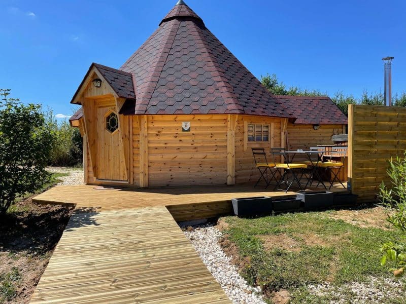 Charmante cabane en bois avec un toit en ardoise et terrasse ensoleillée.