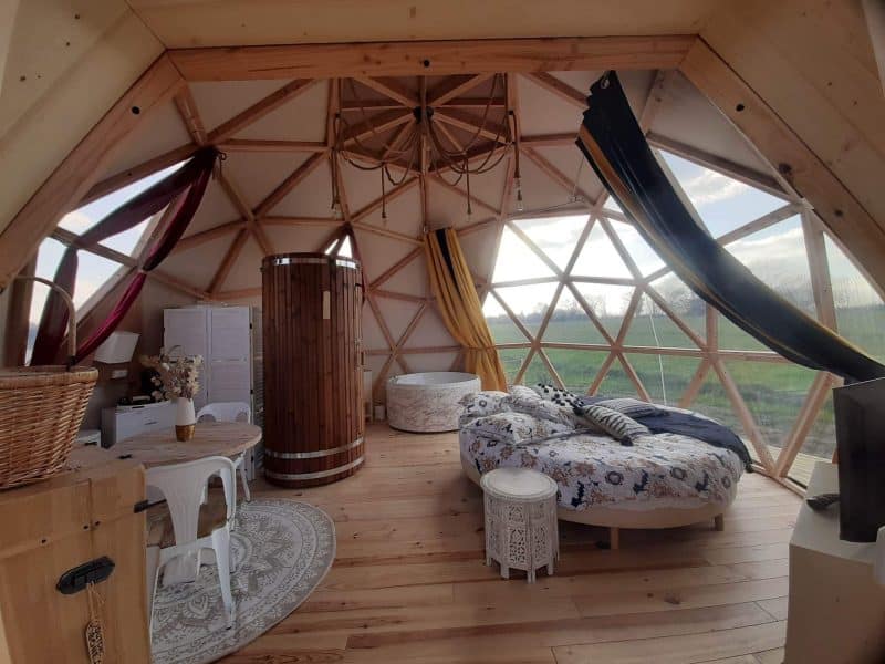 Dôme géodésique avec lit rond, décoré de rideaux colorés et vue sur la nature.
