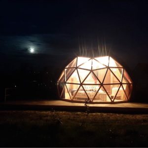 Dôme géodésique lumineux sous la lune, offrant une vue panoramique unique.