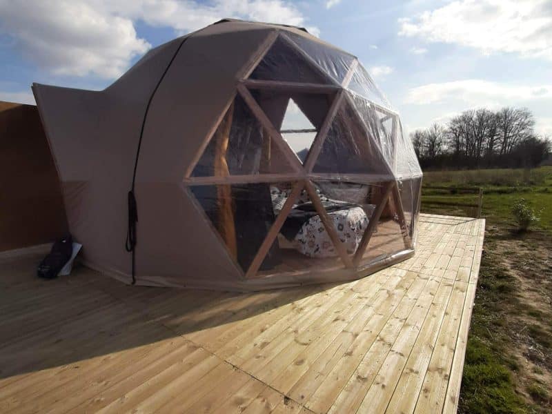 Dôme géodésique sur terrasse en bois, offrant une vue dégagée sur la nature.