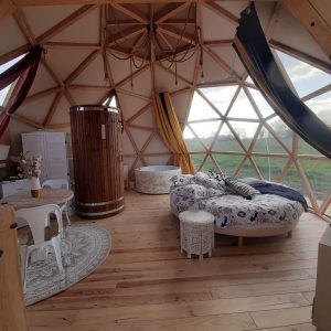 Dôme géodésique lumineux avec lit rond et baignoire en bois, vue sur la nature.