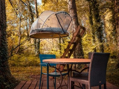 Cabane suspendue dans les arbres, entourée de verdure, avec une terrasse en bois.
