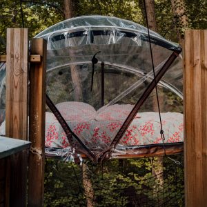 Hébergement insolite : bulle suspendue avec un lit douillet, entourée de verdure.