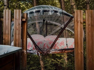 Hébergement insolite : bulle suspendue avec un lit douillet, entourée de verdure.
