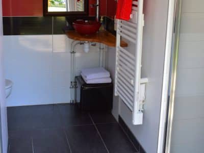 Salle de bain moderne dun hébergement insolite en Nouvelle-Aquitaine, avec des touches rouges.