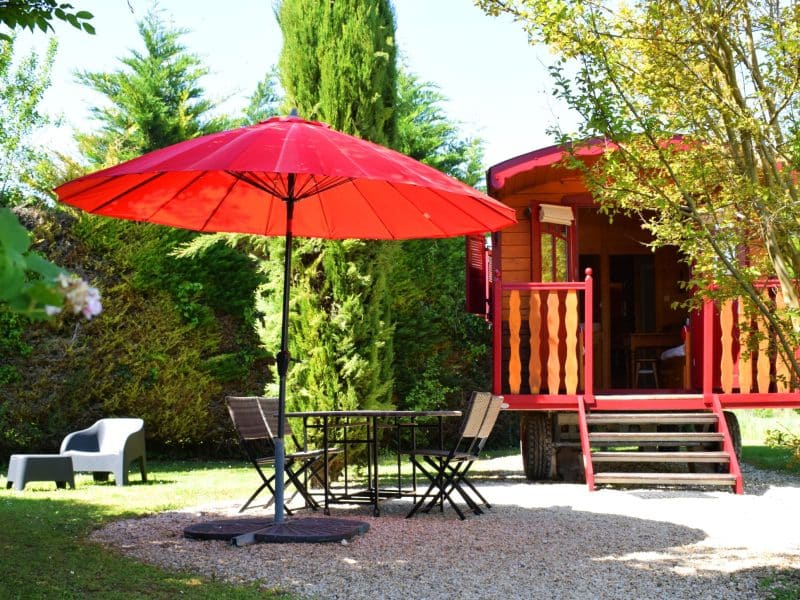 Charmante roulotte en Nouvelle-Aquitaine, avec parasol rouge et terrasse accueillante.
