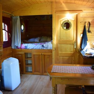 Hébergement insolite en roulotte en bois, intérieur chaleureux avec lit en alcôve.