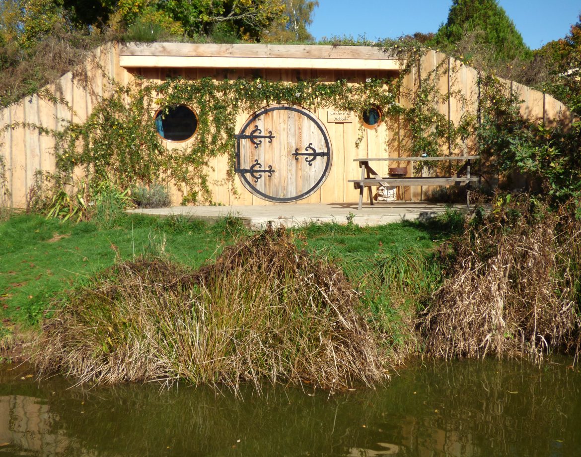 Hébergement insolite en Auvergne : cabane en bois avec porte ronde et vue sur leau.