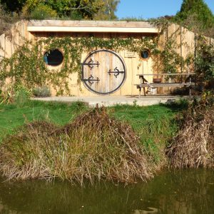 Hébergement insolite en Auvergne : cabane en bois avec porte ronde et vue sur leau.